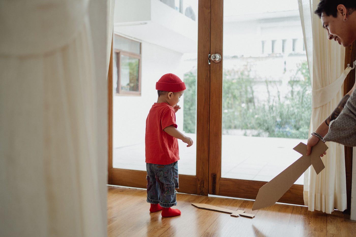 A father and son playing with cardboard swords in a sunny living room