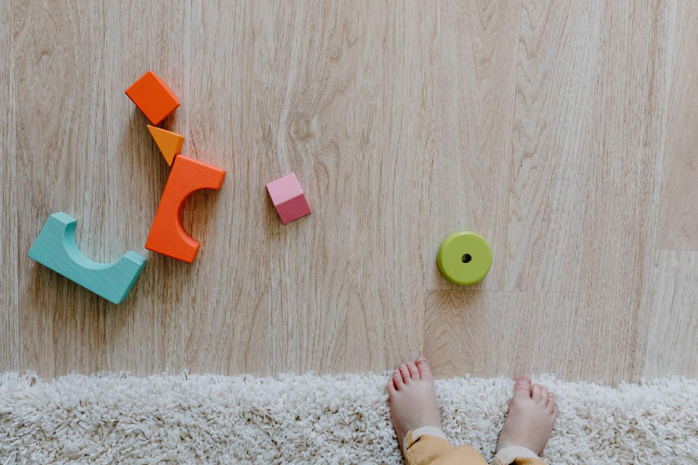 Colorful wooden blocks and baby feet on a carpet and wooden floor