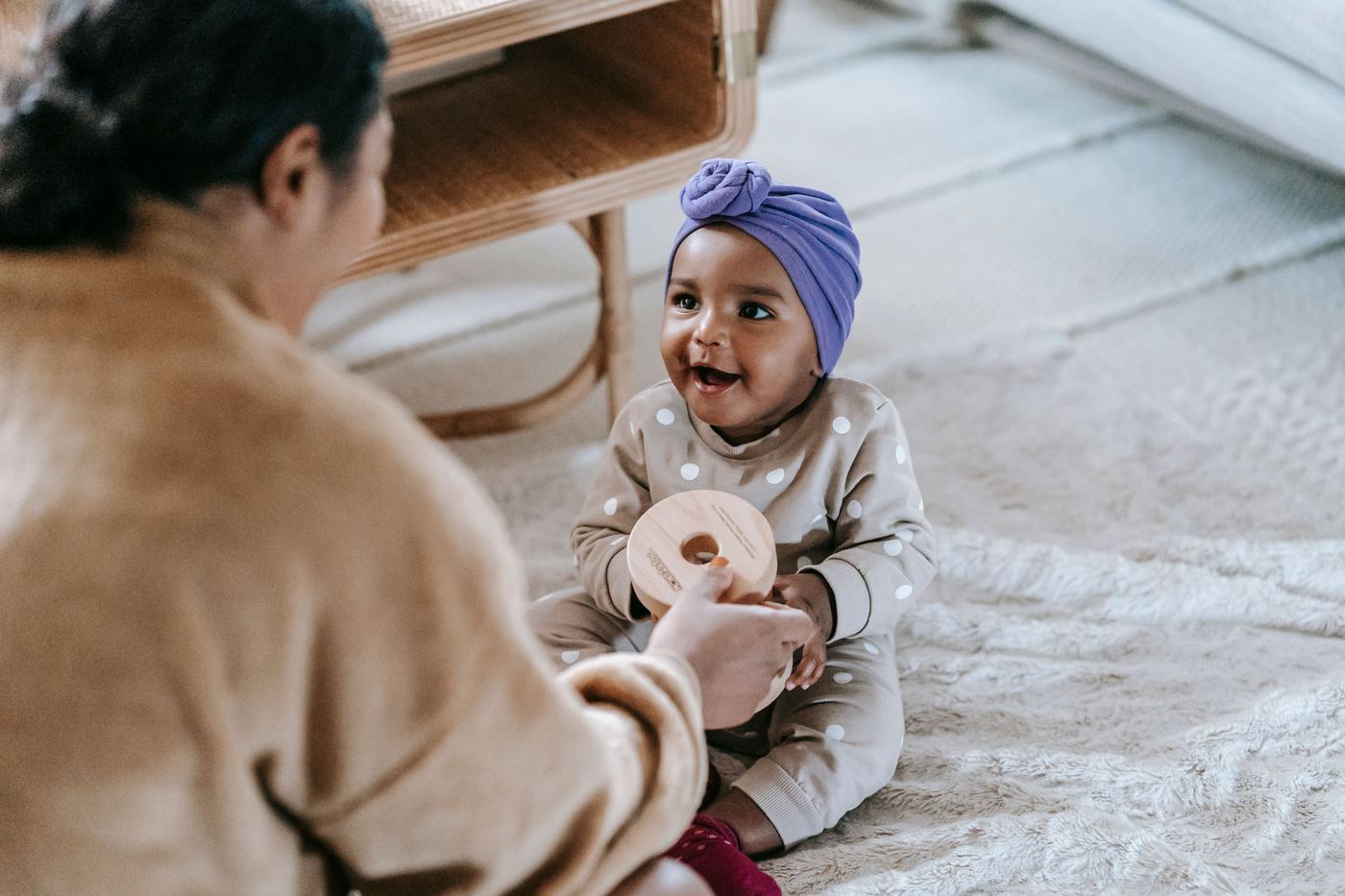 African American mother sitting on floor near little black toddler with wooden toy while spending time in living room at