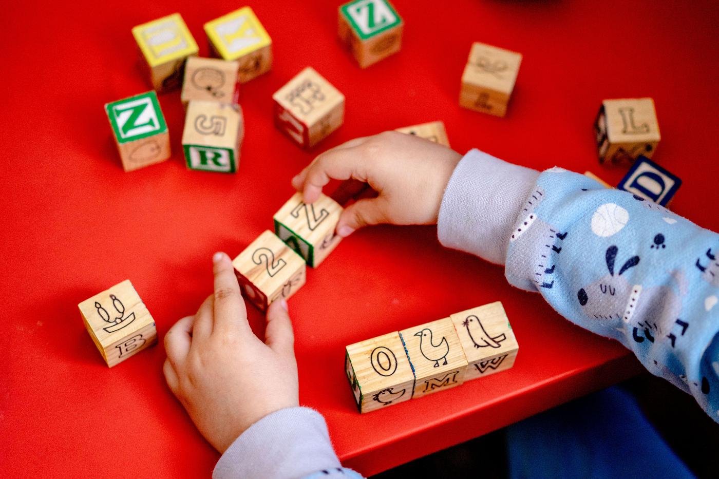 Young child engaging with wooden alphabet blocks on a vibrant red table