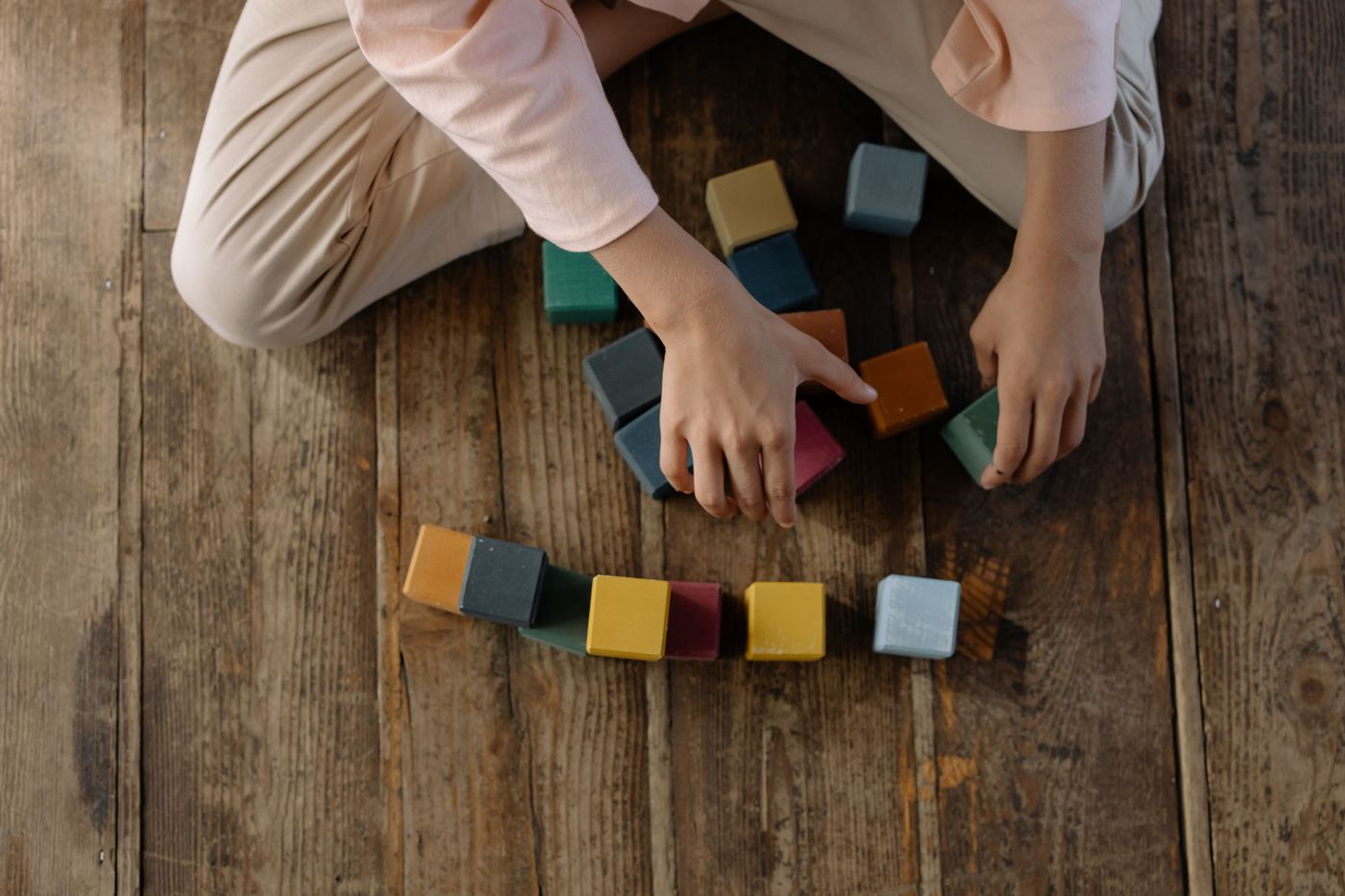 Child arranging colorful toy blocks on a wooden floor