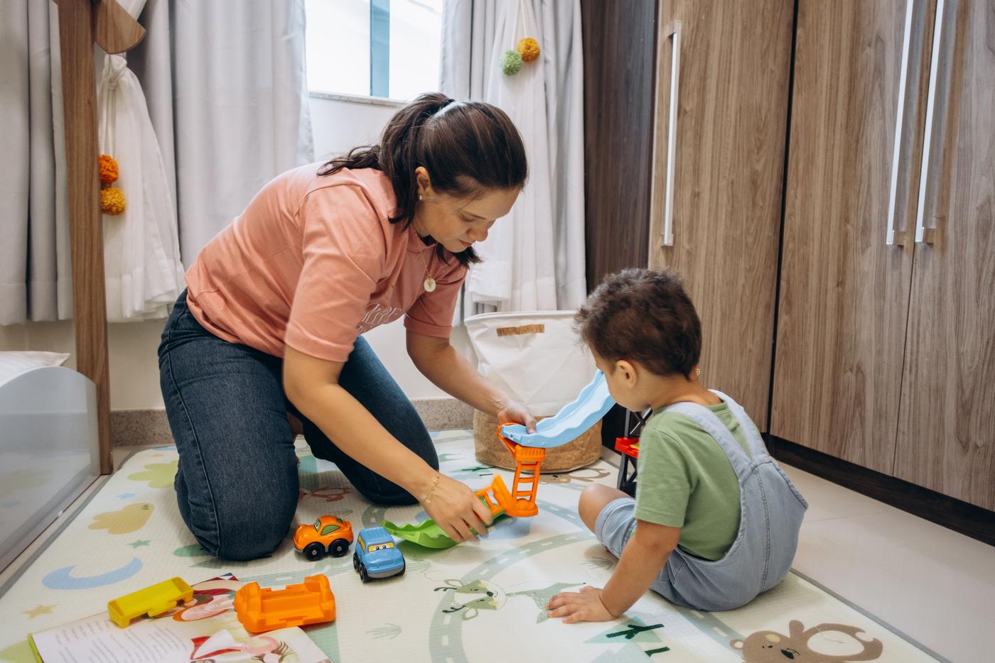 A mother and son enjoy playtime with toy cars on a room floor