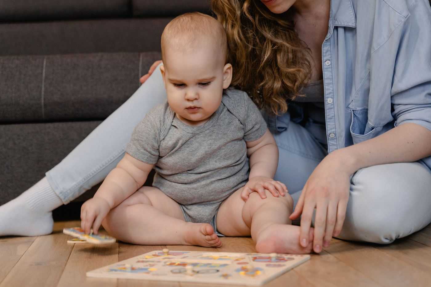 A mother and baby bonding over a wooden puzzle on the living room floor