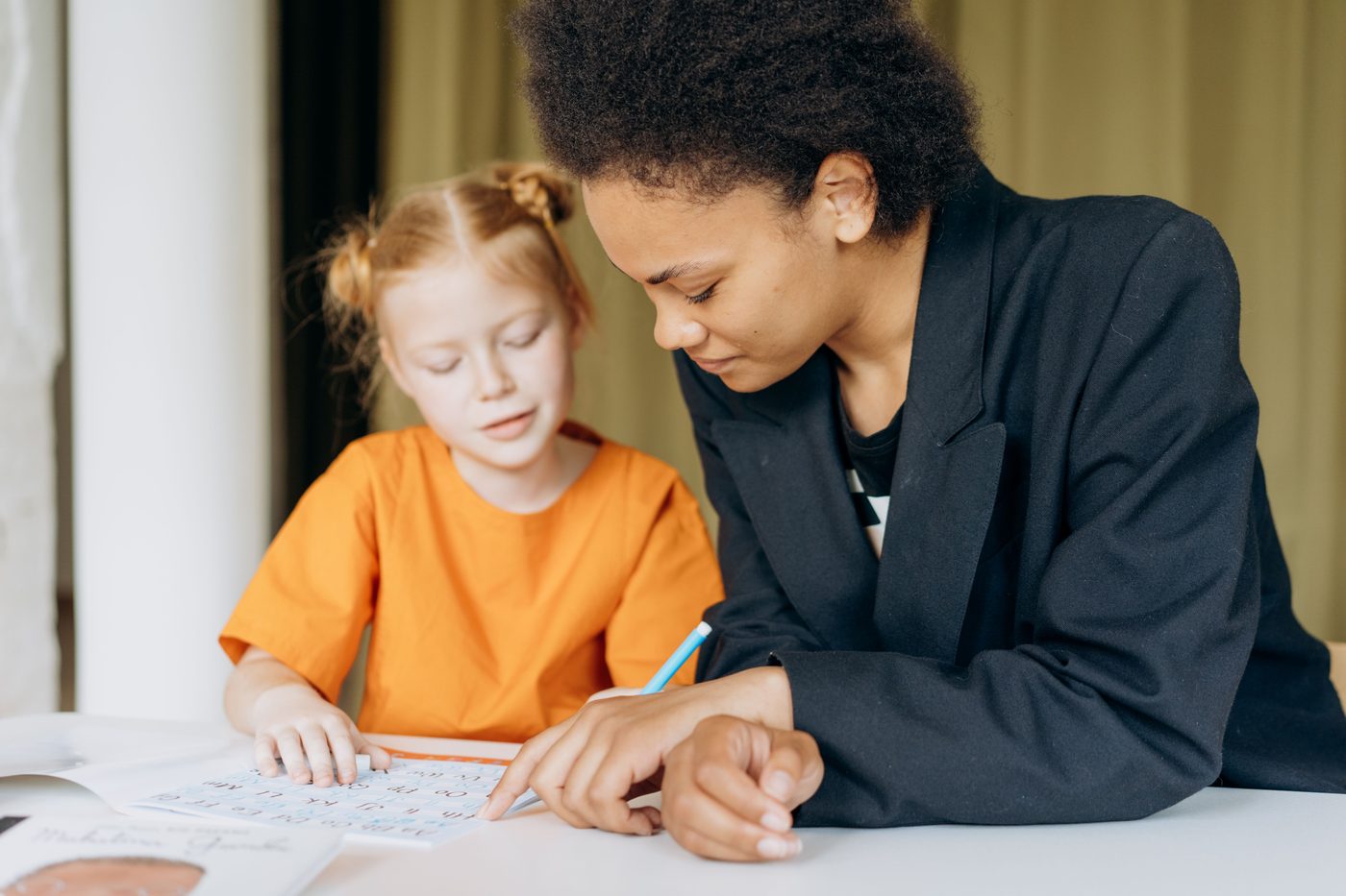 A teacher helps a young student with writing tasks at a desk indoors