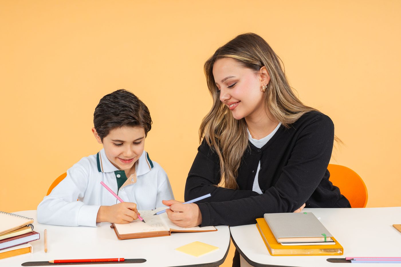 Young teacher helps a schoolboy with writing at a desk