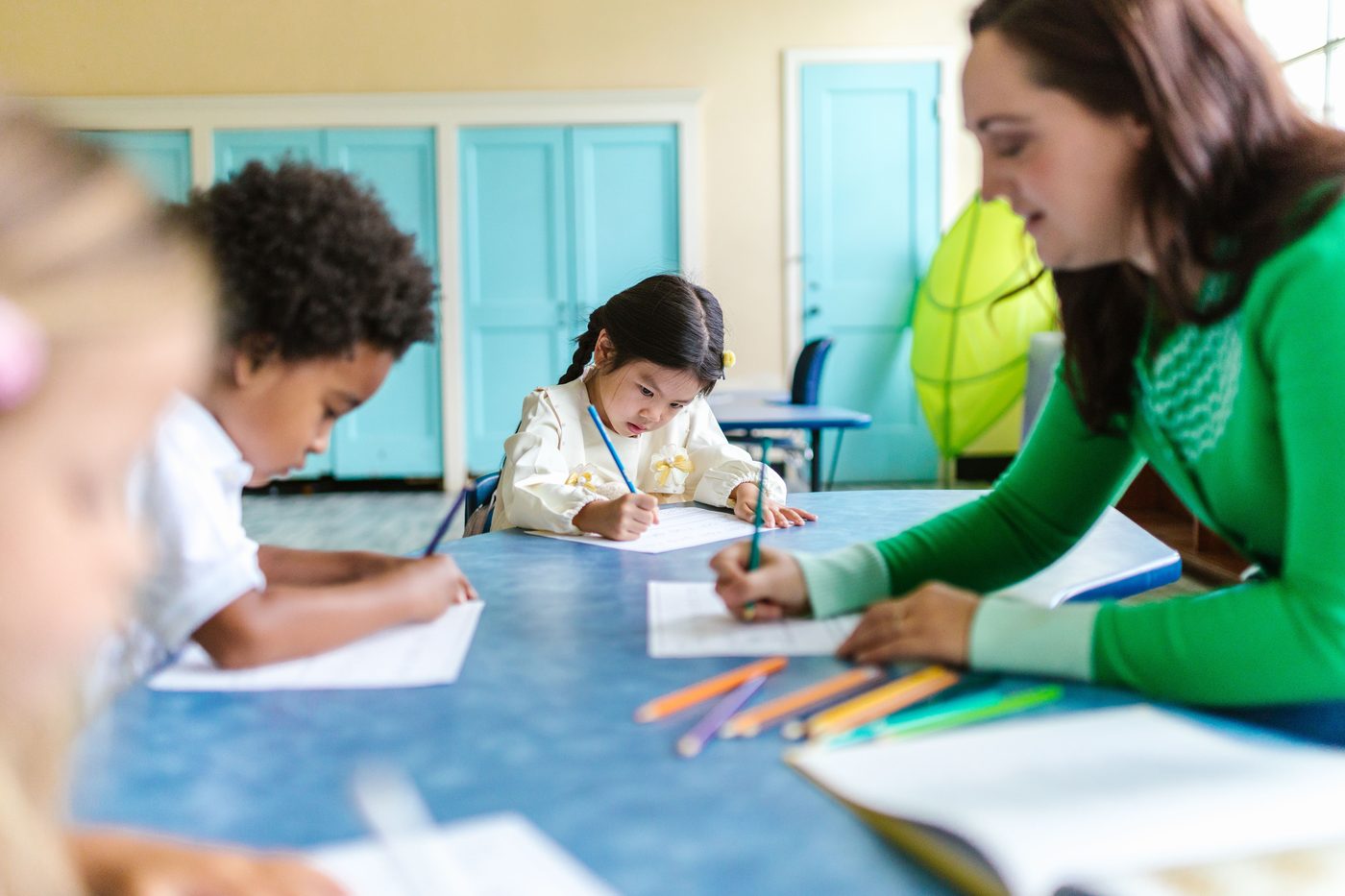 Kids focused on drawing and learning with a teacher's guidance in a bright classroom